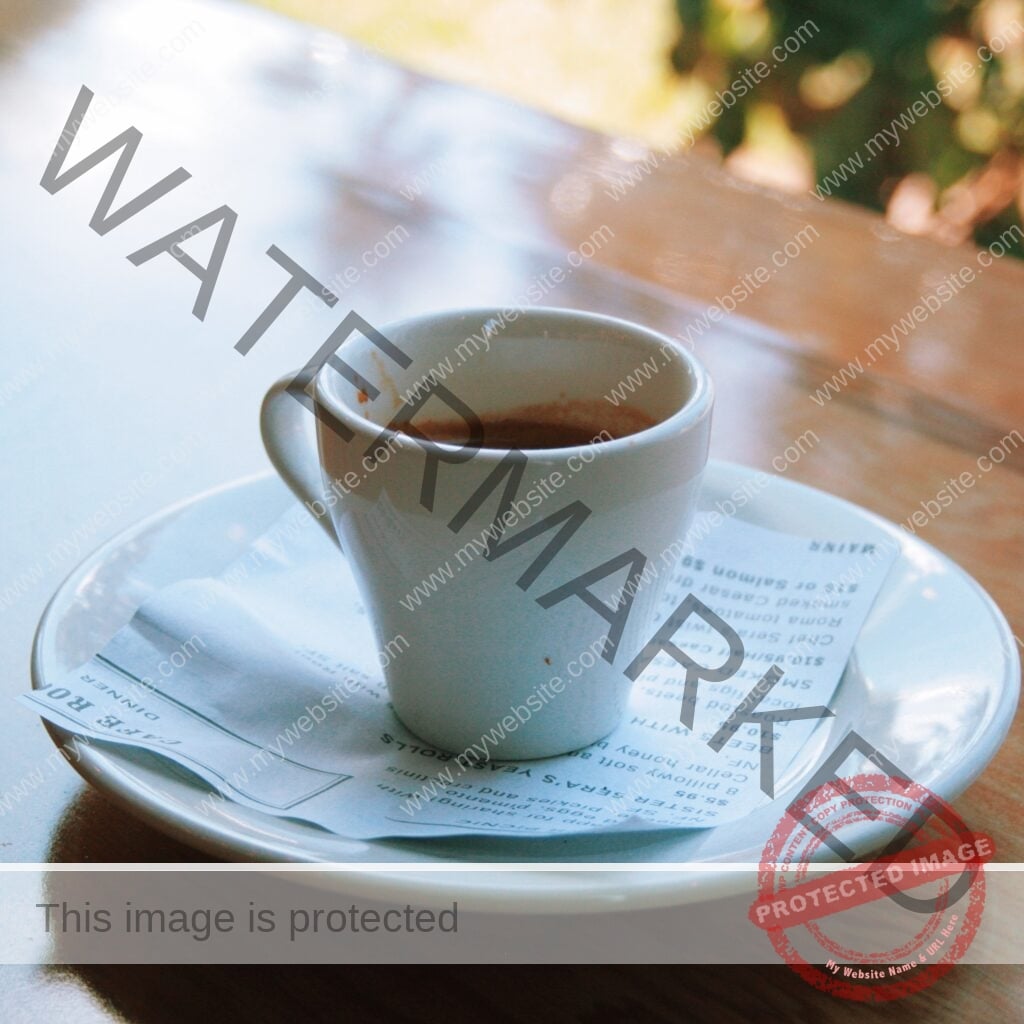 A small white ceramic cup holding a dark espresso sits on a matching white saucer, photographed in warm natural light. The cup and saucer rest on a folded printed paper menu headed "Cafe Root Cellar Dinner," with menu items partially legible beneath. The table has a glossy wood-toned surface, and softly blurred green and golden foliage is visible through a window in the background.