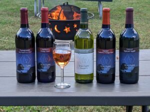 5 bottles of honey wine and 1 glass of honey wine pictured with a campfire in the background. 