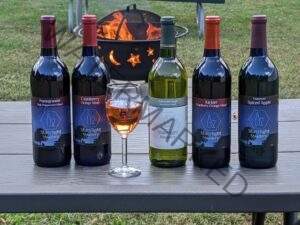 5 bottles of honey wine and 1 glass of honey wine pictured with a campfire in the background. 