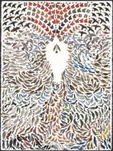 A large mixed-media collage artwork densely packed with hundreds of small bird silhouettes cut from textured and patterned papers in muted natural tones — browns, grays, blacks, soft blues, ochre yellows, deep reds, and creams. The birds are arranged in swirling, radiating formations that flow outward from a central white negative-space opening shaped like a single bird in flight. Around this empty silhouette, the surrounding birds appear to spiral and ripple in concentric waves, with rows of red-winged birds forming an arched canopy across the top of the composition and denser, darker clusters massing at the bottom edge. Each bird is rendered as a simple cut-paper shape with a small round eye, but the variety of paper textures gives the flock individual character. The piece sits on a torn-edge sheet of cream paper against a black background.