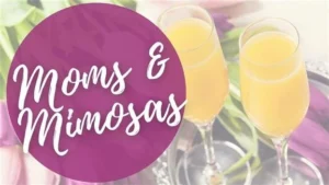 Promotional graphic reading "Moms & Mimosas" in white script on a purple circle, set against a soft-focus background of two champagne flutes filled with mimosas on a silver tray with pink flowers.