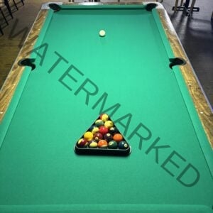 Top-down view of The Place to Be's pool table, with bright green felt and dark wood rails. All 15 numbered balls are racked tightly in the black plastic triangle near the foot of the table, and the white cue ball sits placed for the break. Cue sticks and chairs are visible at the edges of the frame.