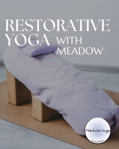 A promotional graphic for a Pittsboro Yoga class titled "Restorative Yoga with Meadow" in white text across the top. The image shows a restorative yoga setup: a lavender bolster and matching pillow arranged at an incline, supported underneath by two cork yoga blocks, resting on a cork-colored mat over a pale floor. The setting is soft and minimal, suggesting a calm studio space. The round Pittsboro Yoga logo appears in the lower-right corner.